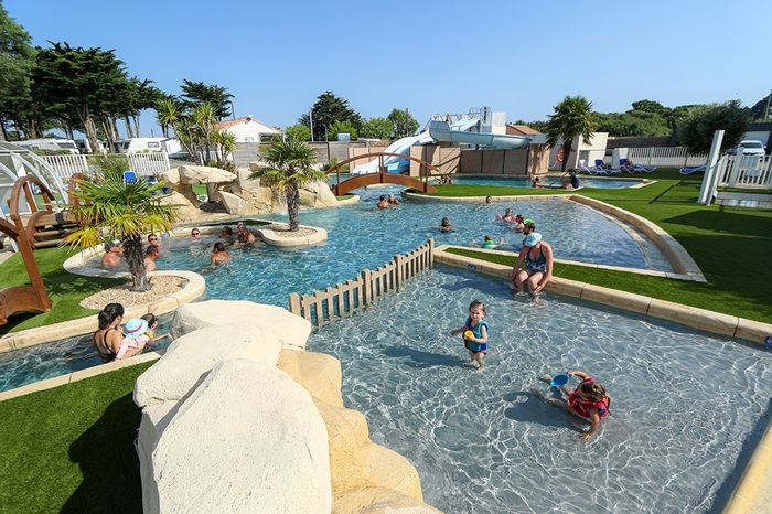 Pataugeoire ludique et bassin extérieur avec enfants qui jouent, entourés de palmiers au camping Mirabel La Renaudière.