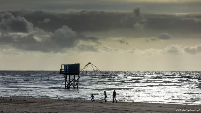Bord de mer avec des enfants jouant sur la plage ainsi qu'une ancienne cabane de pêche